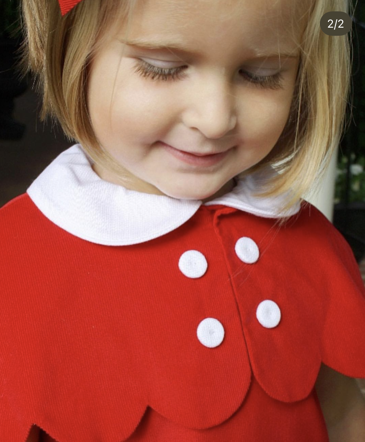 Close-up of a child wearing a red dress with white buttons and collar.