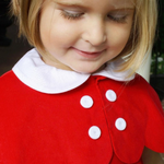 Close-up of a child wearing a red dress with white buttons and collar.