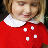 Close-up of a child wearing a red dress with white buttons and collar.
