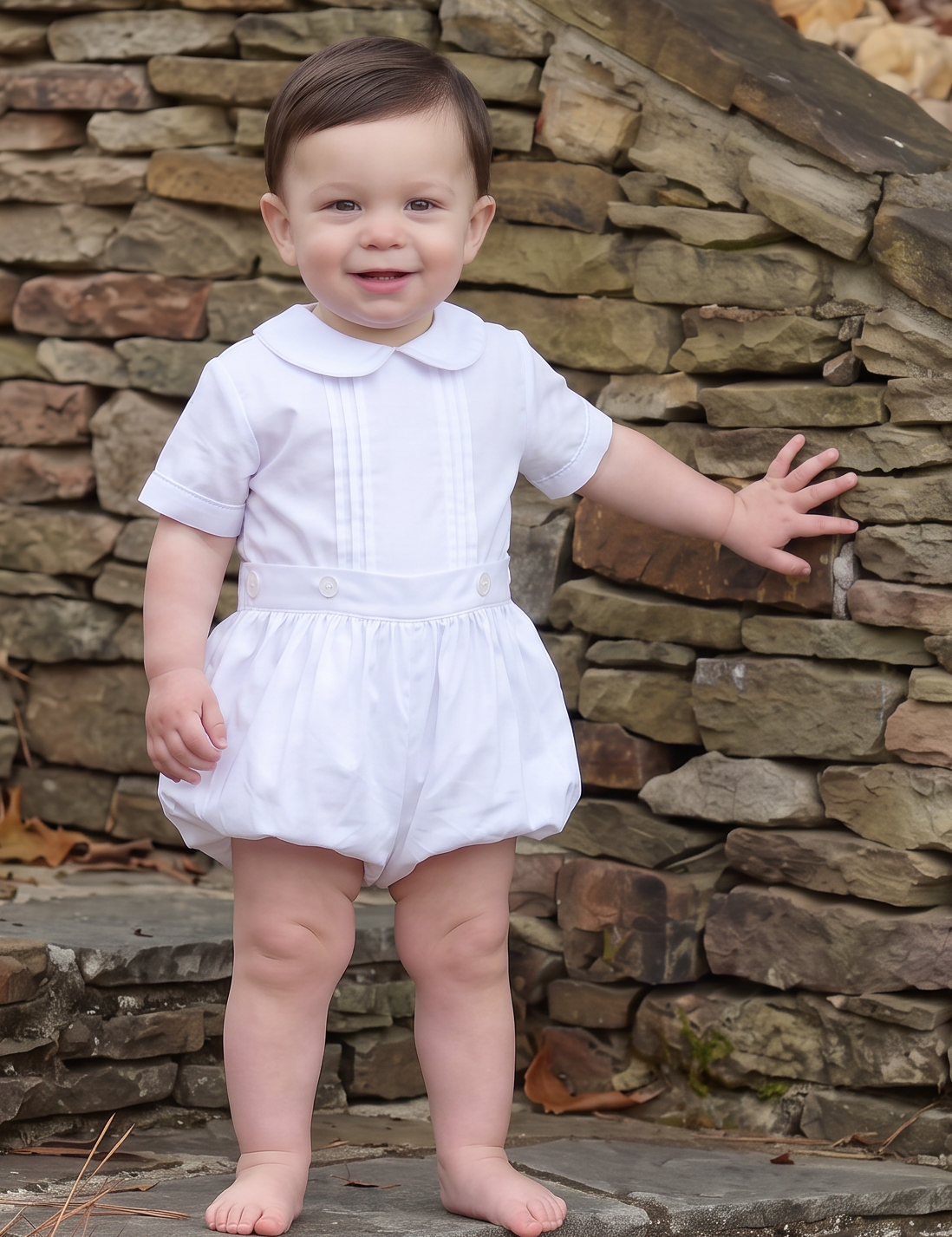 A toddler standing barefoot on stone steps outdoors, wearing a white short-sleeve romper dress with a Peter Pan collar.