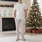 Man wearing Christmas-themed pajama pants standing in a living room with a decorated tree and fireplace.
