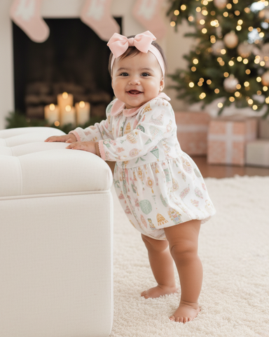 Baby in a floral dress standing in a festive living room with Christmas decorations.