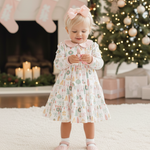 Young girl in a floral dress standing in front of a Christmas tree and fireplace.