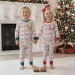 Two children in matching pajamas standing in front of a Christmas tree and fireplace.