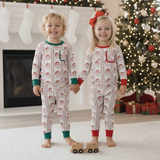 Two children in matching pajamas standing in front of a Christmas tree and fireplace.