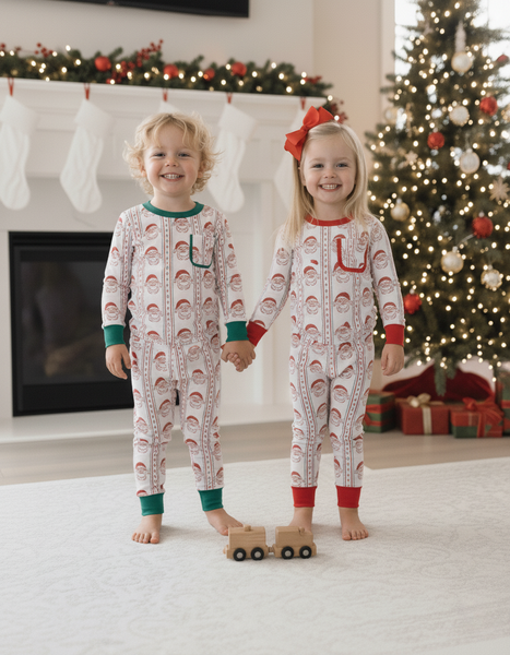 Two children in matching pajamas standing in front of a Christmas tree and fireplace.