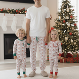 Family of three wearing matching pajamas in a festive living room with a Christmas tree and fireplace.