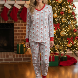 Woman wearing Christmas-themed pajamas in front of a decorated fireplace and tree.