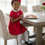 Young girl in a red dress sitting at a table with cookies, smiling.