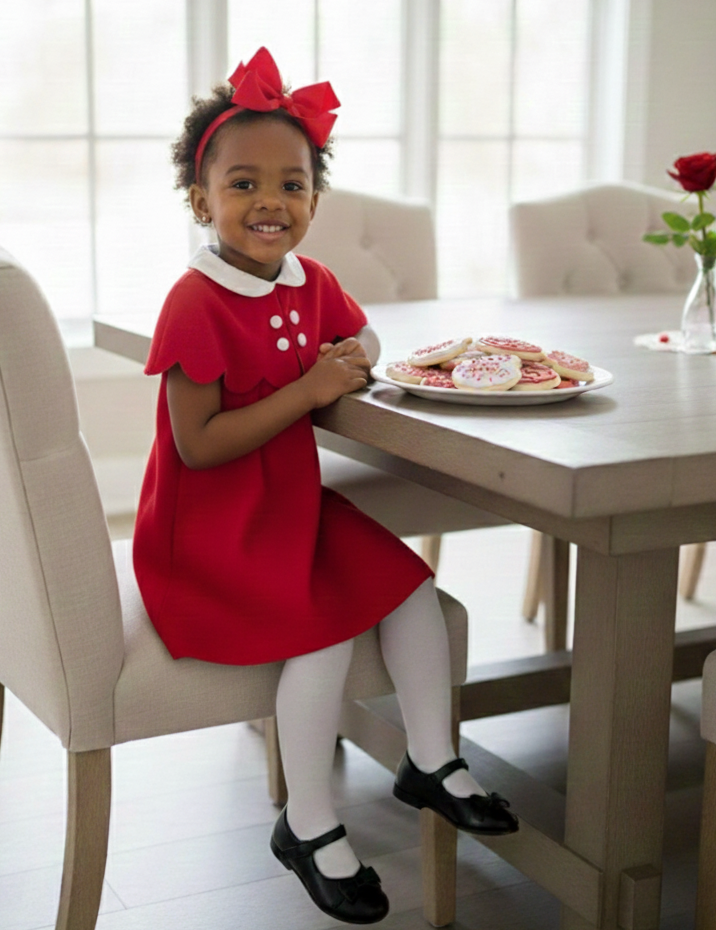 Young girl in a red dress sitting at a table with cookies, smiling.