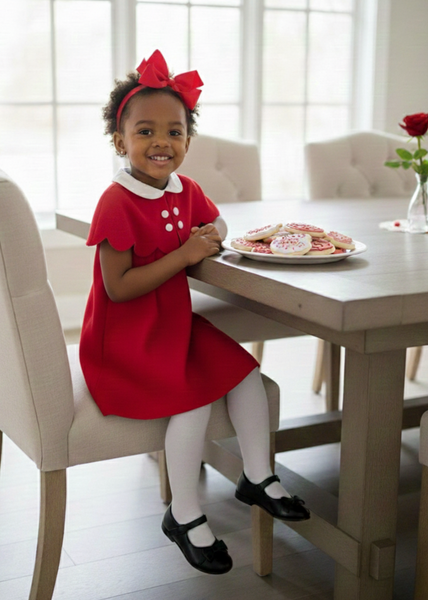 Young girl in a red dress sitting at a table with cookies, smiling.